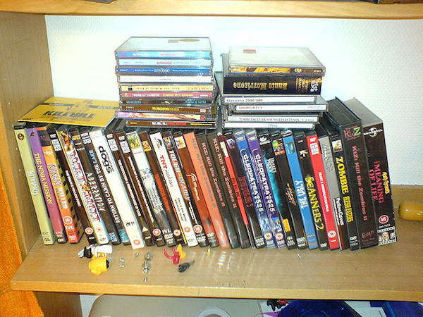 A small collection of old CDs and DVDs are gathering dust on a wooden shelf