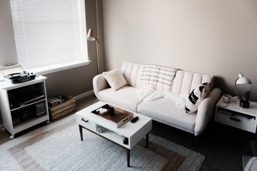 a clean apartment with white walls and a white sofa, end table, coffee table, and rolling shelving unit