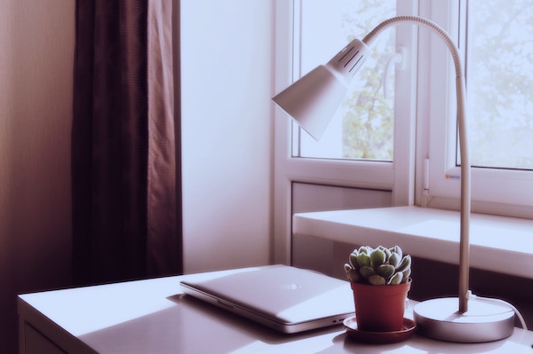 a macbook on a home office desk next to a window that's letting in a lot of natural light