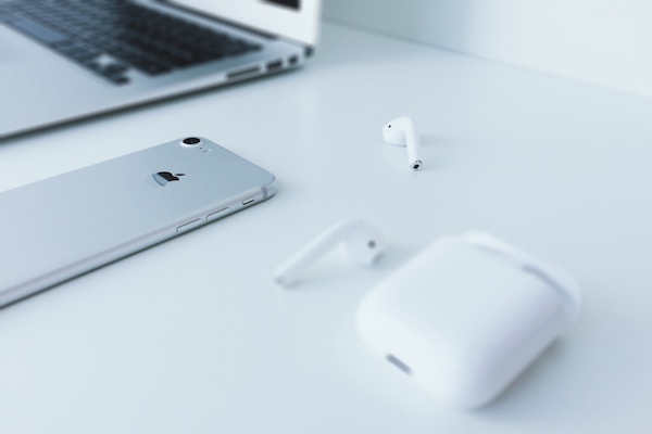 airpods are next to an iphone and a macbook air on a white home office desk