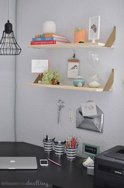 2 floating shelves are storing various household items above an organized desk and office supplies