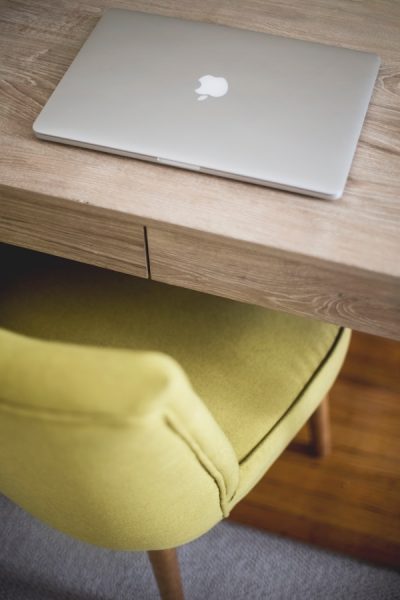 a comfy chair is pushed in underneath a wooden desk with a laptop