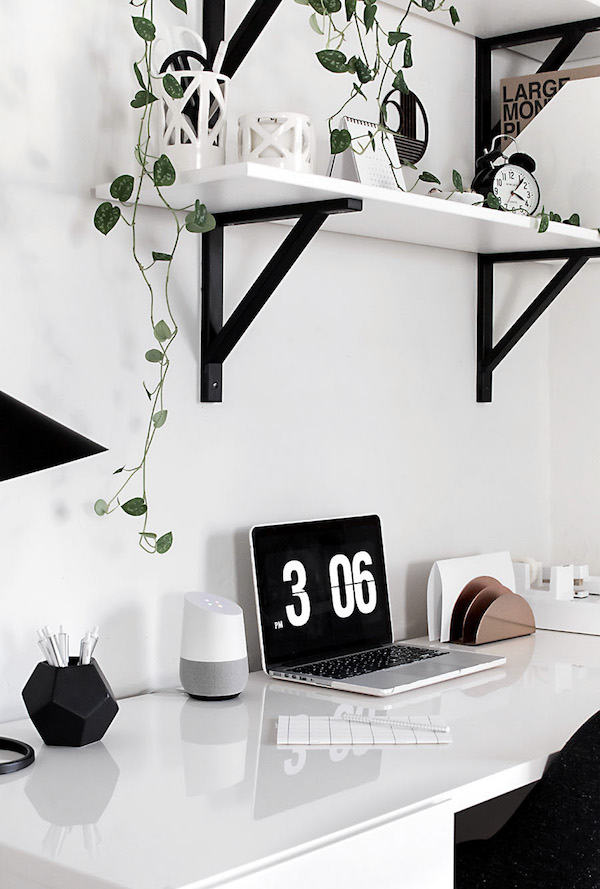 the tendrils of a houseplant hanging over a clean home office desk, google home smart speaker, and laptop