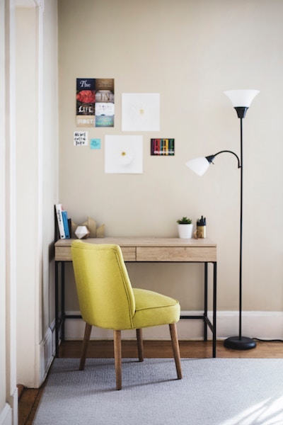 a clean and tidy desk sits next to a tall lamp and chair in a home