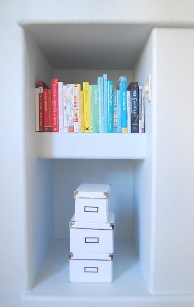 books are lined up in a small nook, under which is a stack of three storage boxes