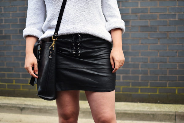 a girl wearing a black leather tie front mini skirt and a black bag over her left shoulder
