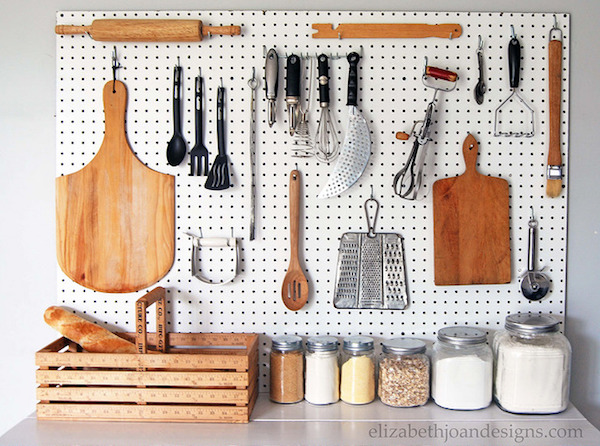 a pegboard hangs in the kitchen with cooking supplies like a cutting board and knives