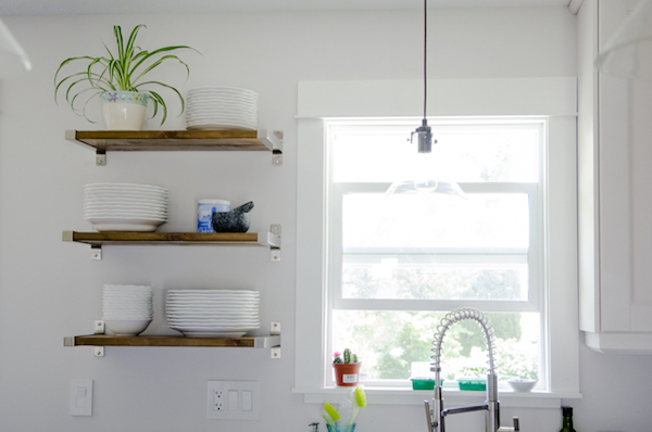 floating shelves hold plates and a plant near a window in a white kitchen