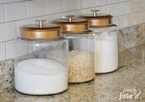 three clear canisters with gold lids hold flour, sugar, and oats