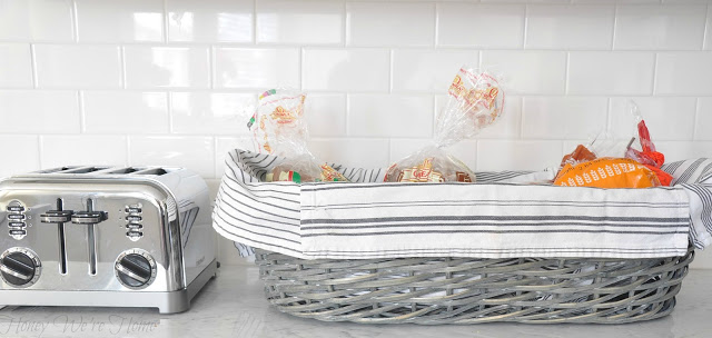 a grey wicker basket lined with a white towel holds three loaves of packaged bread