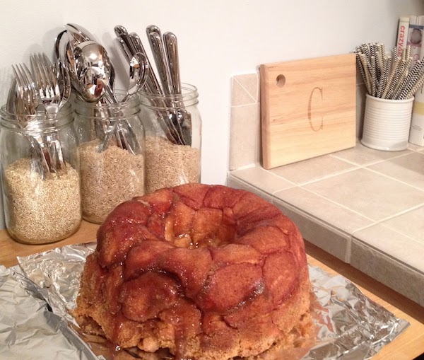 three mason jars are filled with spoons, forks, and knives on a countertop behind a loaf of monkey bread