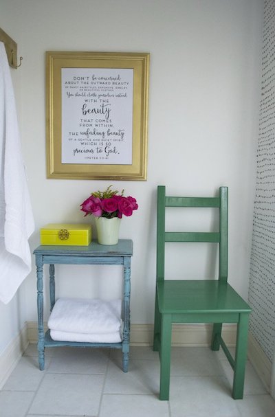 a poem in a gold picture frame above a blue side table next to a green chair in a bathroom