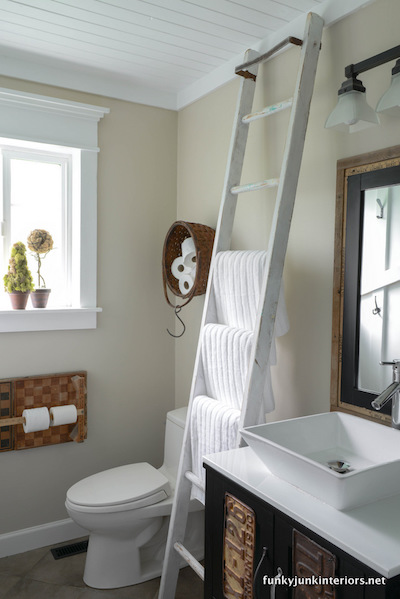 3 white towels on rungs of an old white ladder leaning against a bathroom wall