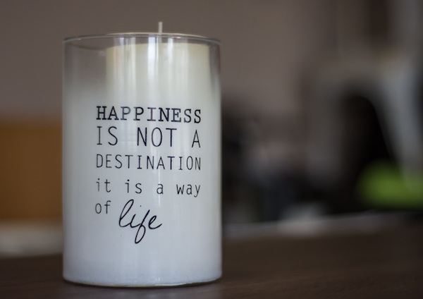 white candle in a glass candle holder that reads "happiness is not a destination it is a way of life" 