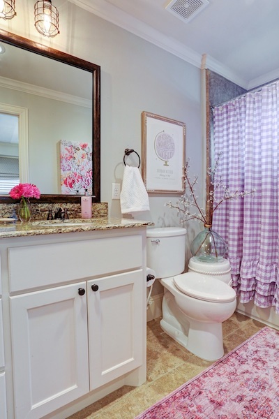a perky bathroom with a pink shower curtain and flowers on the counter