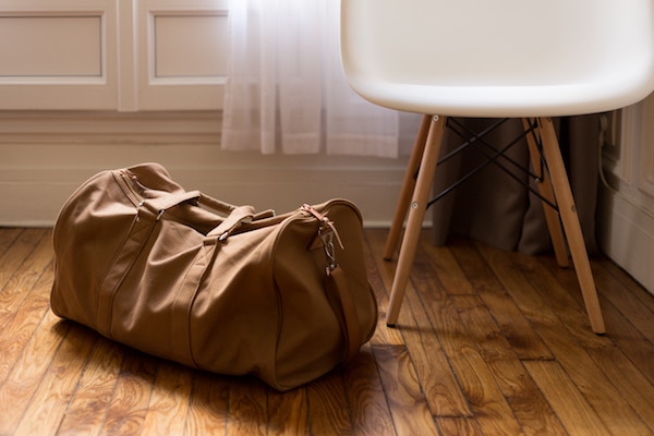 a canvas overnight bag lies next to a white chair