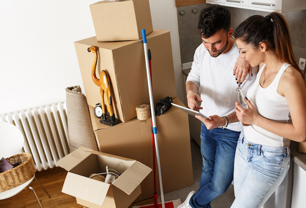 Young couple moving in new apartment. Standing by the kitchen and using tablet.