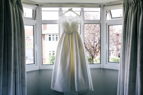 a single wedding dress hangs near a window