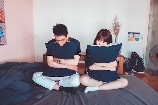 couple sitting on bed hugging pillows