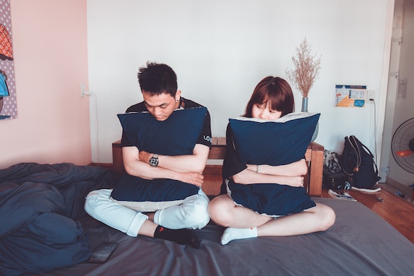 couple sitting on bed hugging pillows