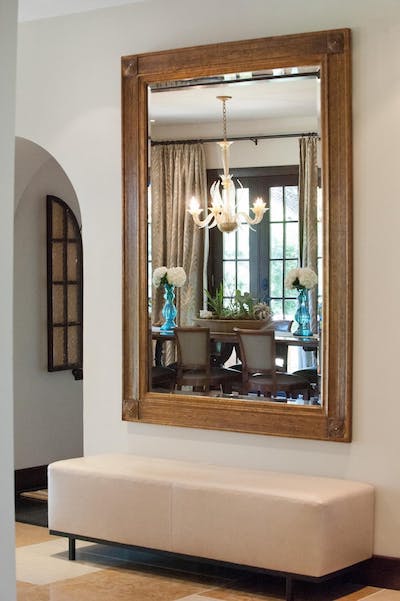 large wood mirror reflecting light from chandelier and window