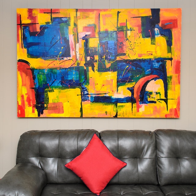a bright abstract painting above a brown leather couch