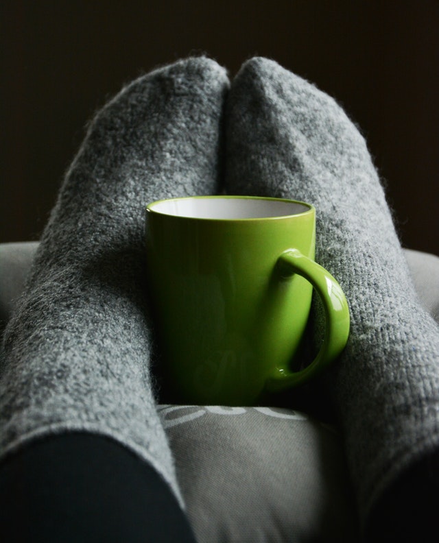 feet in warm fuzzy socks against a cup of warm beverage