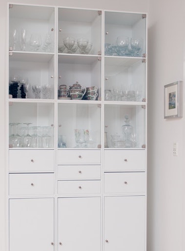 A neatly organized kitchen cabinet with glasses, bowls, and vases