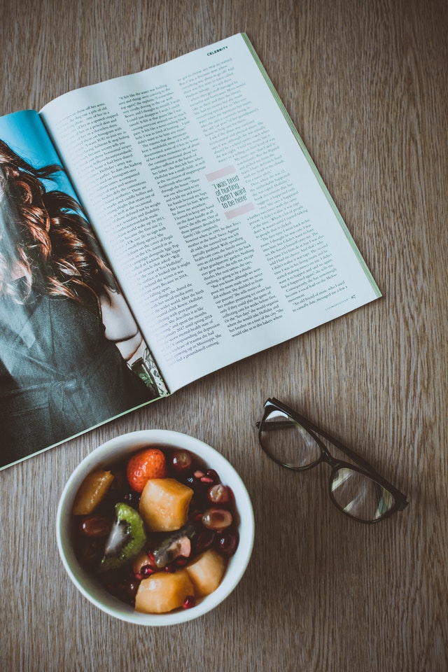a magazine, a bowl of fruit and a pair of sunglasses on a tabletop