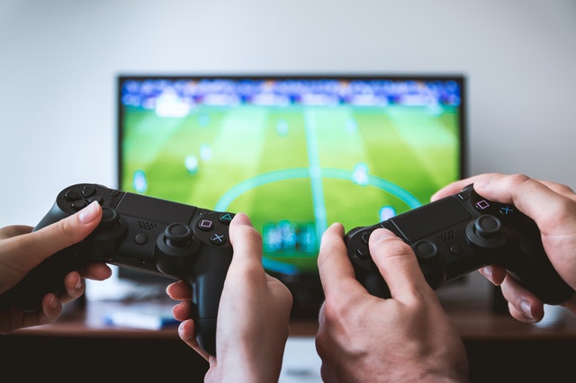 Two hands holding joysticks against a TV screen 