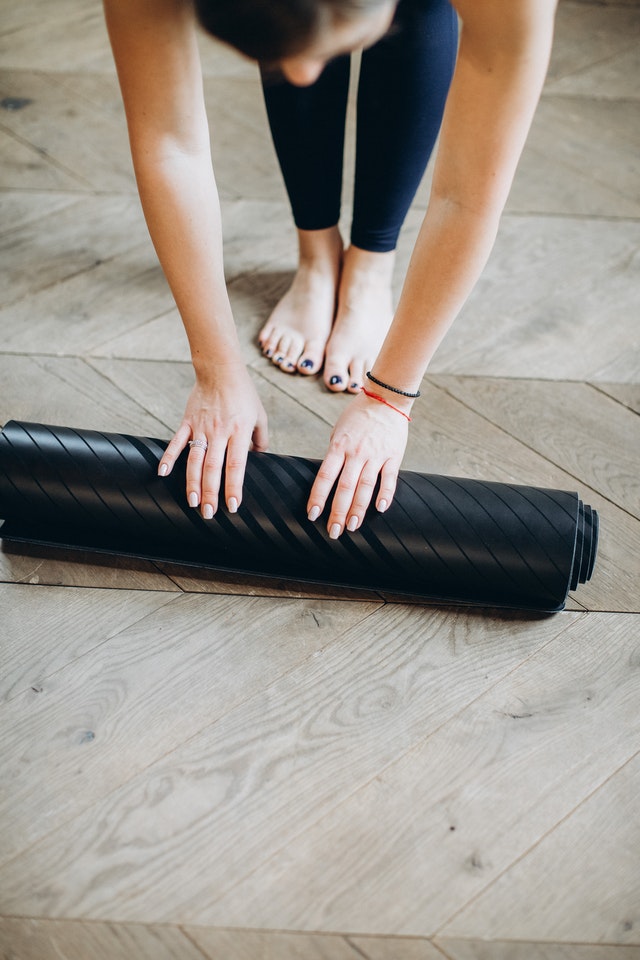 A girl rolling up her exercise mat off the floor. 