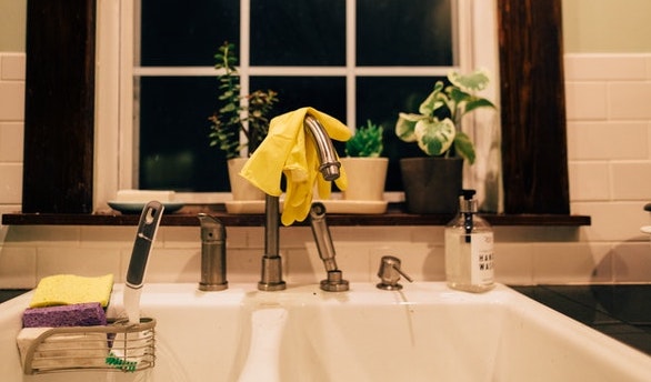 A kitchen sink with gloves hanging on top the faucet