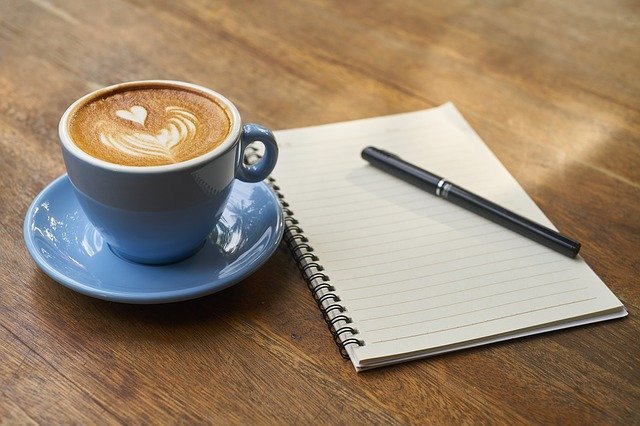 A cup of coffee next to a notebook on a wooden table