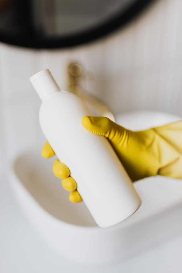 A cleaning bottle in the hands of a person wearing yellow cleaning gloves