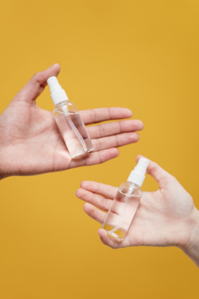 Two hands holding two clear spray bottles 