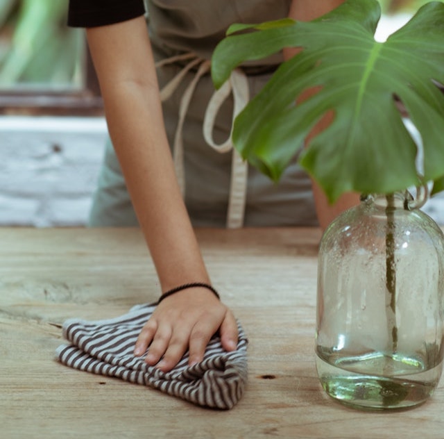 A hand cleaning a wooden table with a damp cloth