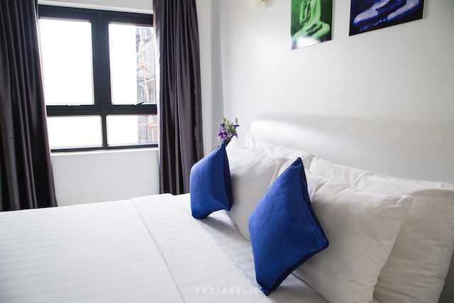 A clean bedroom with blue pillows and a plenty of sunlight