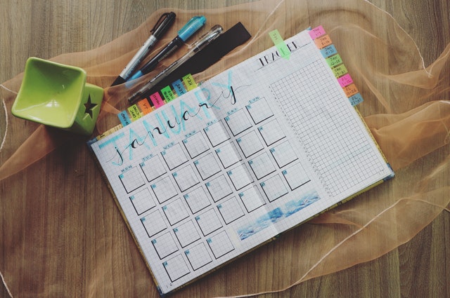 A calendar laying on top of a fabric with markers. 