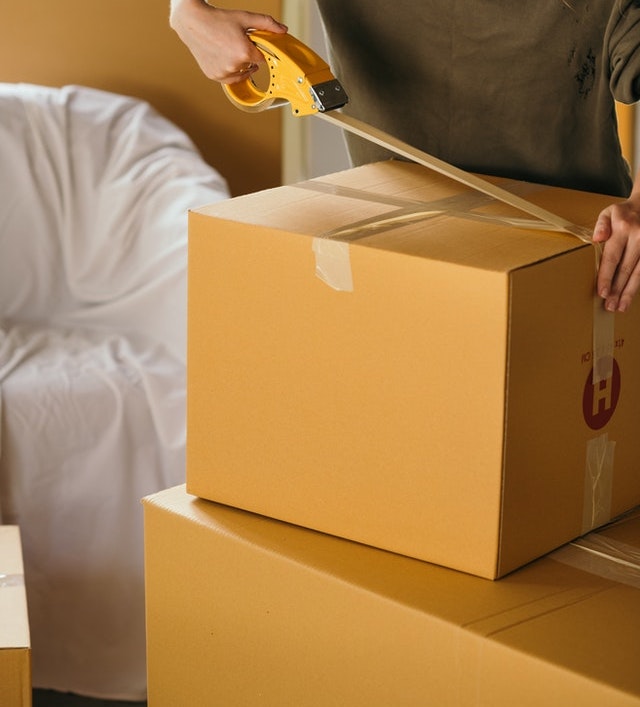 Two hands putting tape on a cardboard box. 