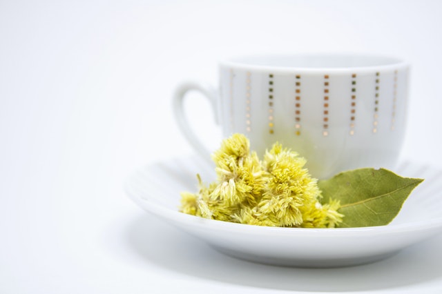 A white cup of tea with yellow flowers in the saucer.