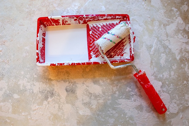 A paint roller in a bucket on the floor. 