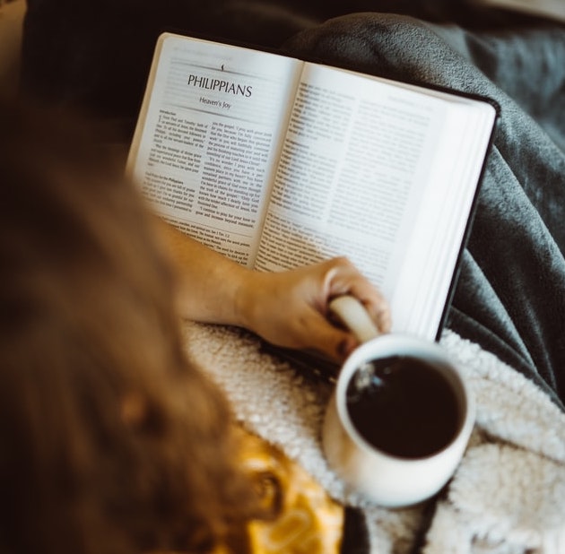 One hand holding a hot beverage with a book in the other hand