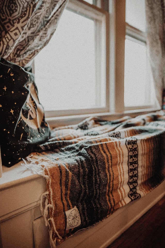 A nook by the window with a pillow, curtains and a warm blanket