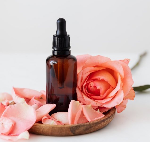 a bottle of an essential oil with dropper surrounded by a pink rose and its petals