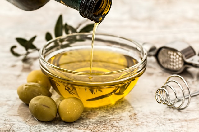 A bowl of olive oil surrounded by fresh olives