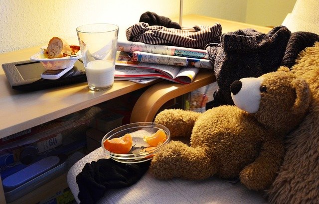 A teddy bear lying around with a half glass full of milk, oranges and books strewn around it.