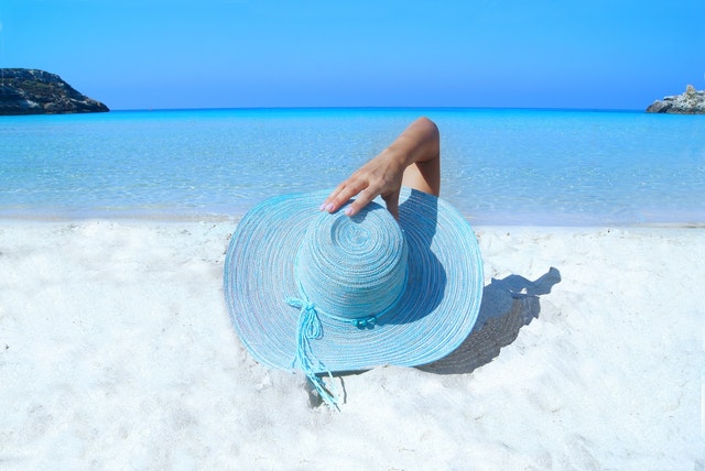 A girl laying on the beach with a big blue sun hat