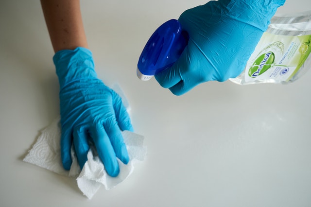 A pair of hands in blue gloves spraying disinfectant on a countertop.