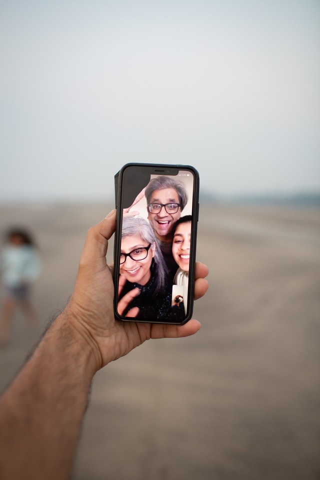 A hand holding . a phone while the phone screen shows a family call in progress.