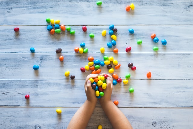 A child's hands arranging colorful candy on a wooden background. 